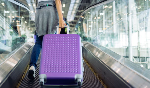 Person seen from the waist down pulling a purple suitcase in an airport
